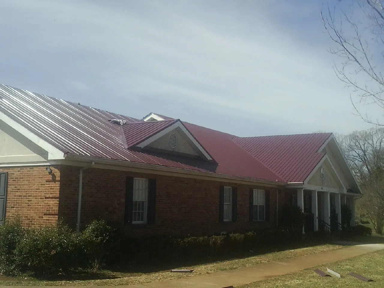 Red metal roof with gabled entries on a long brick building, from a Hail Damage Roof Repair job in Jeffersonville